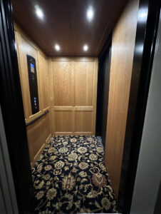 Full interior view of Garaventa Lift home elevator in Iowa City, IA with wood walls, ceiling lights, and patterned carpet