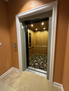 Wide entrance view of Garaventa Lift home elevator in Iowa City, IA with open doors and illuminated wood interior