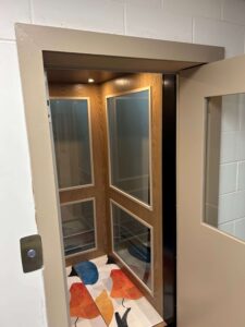 Residential elevator cab with wood-panelled walls, windows and handrail