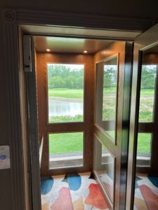 Interior of a windowed home elevator with views of the backyard and golf course