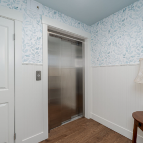 Stainless steel home elevator at the end of a wood-floored hallway in an Edmonds, WA home